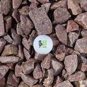 A while golf ball with the OSM logo on a bed of purple-brown stones