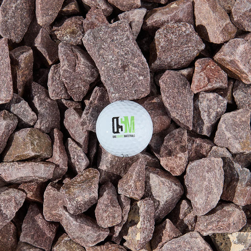 A while golf ball with the OSM logo on a bed of purple-brown stones