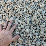 A hand is laid across gravel to illustrate the size of the rocks