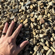 A hand is laid across gravel to show the size of the small stones