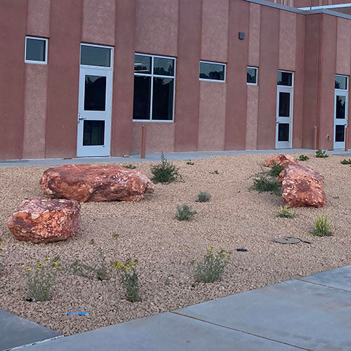 Autumn red boulders and small plants in a gravel bed in front of a building with a brown facade.