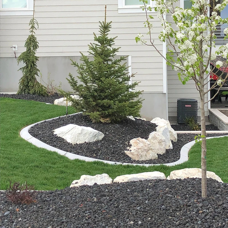Lawn with garden bed featuring rocks, plants, and a small tree in front of a house.