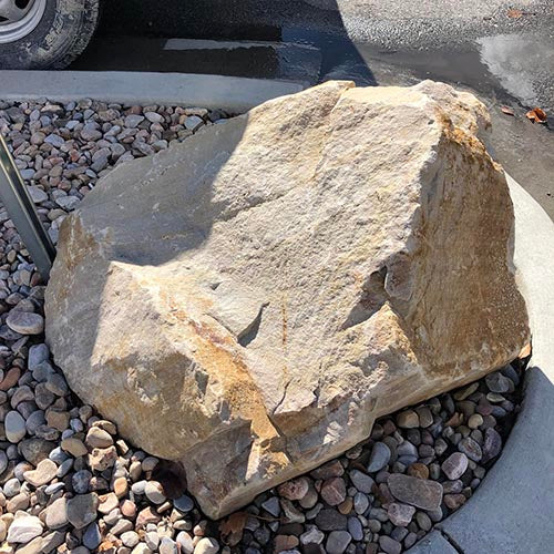 Large browns boulder on a bed of smaller stones with a vehicle tire in the background