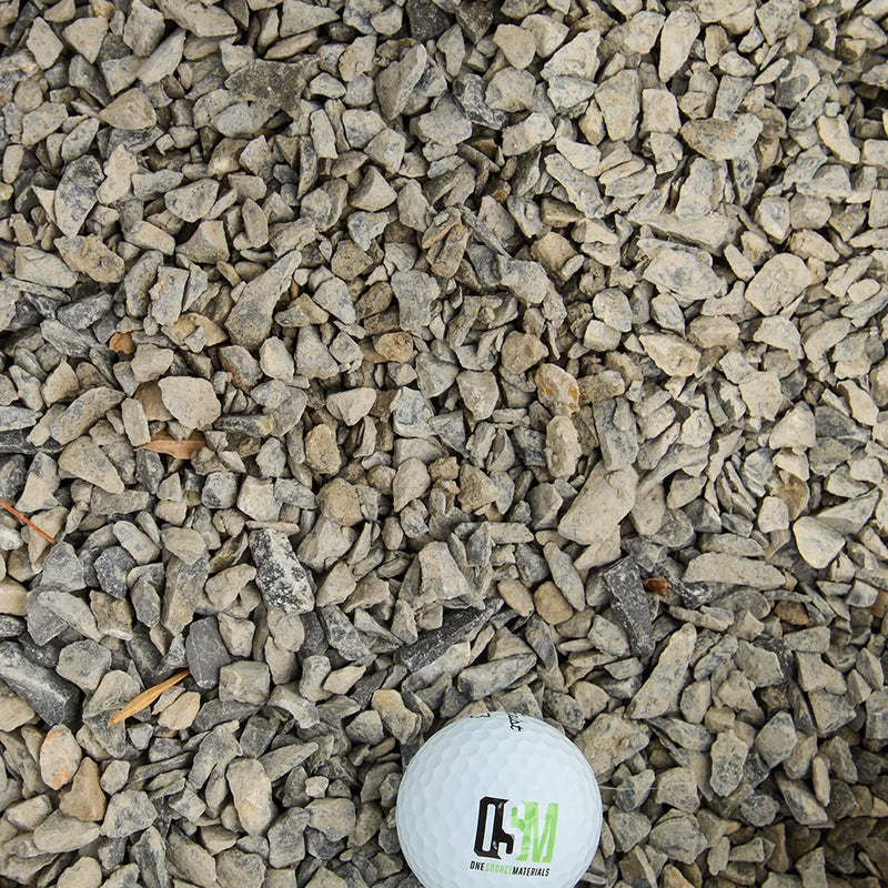 Small stones with a golf ball for scale on a gravel surface, featuring a brand logo.