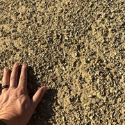 A hand touching crusher fines to illustrate the size of the material