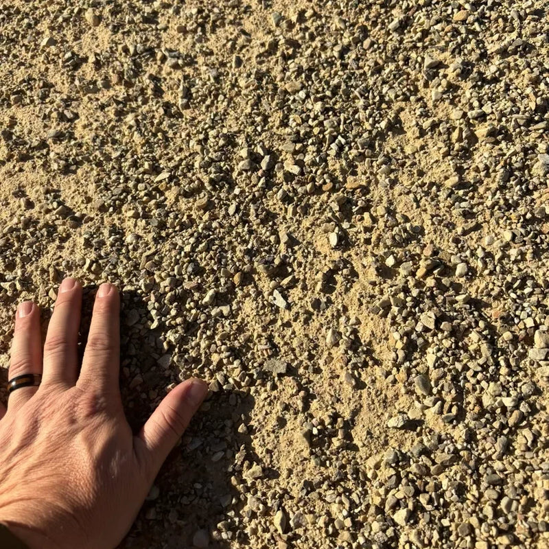 A hand touching crusher fines to illustrate the size of the material