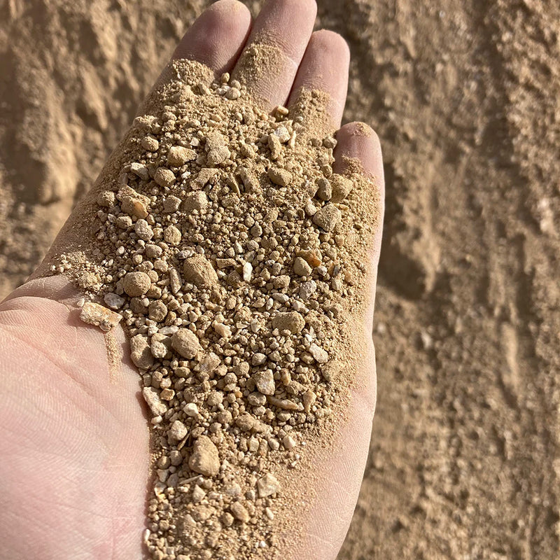 Hand holding a small amount of fines against a sandy background
