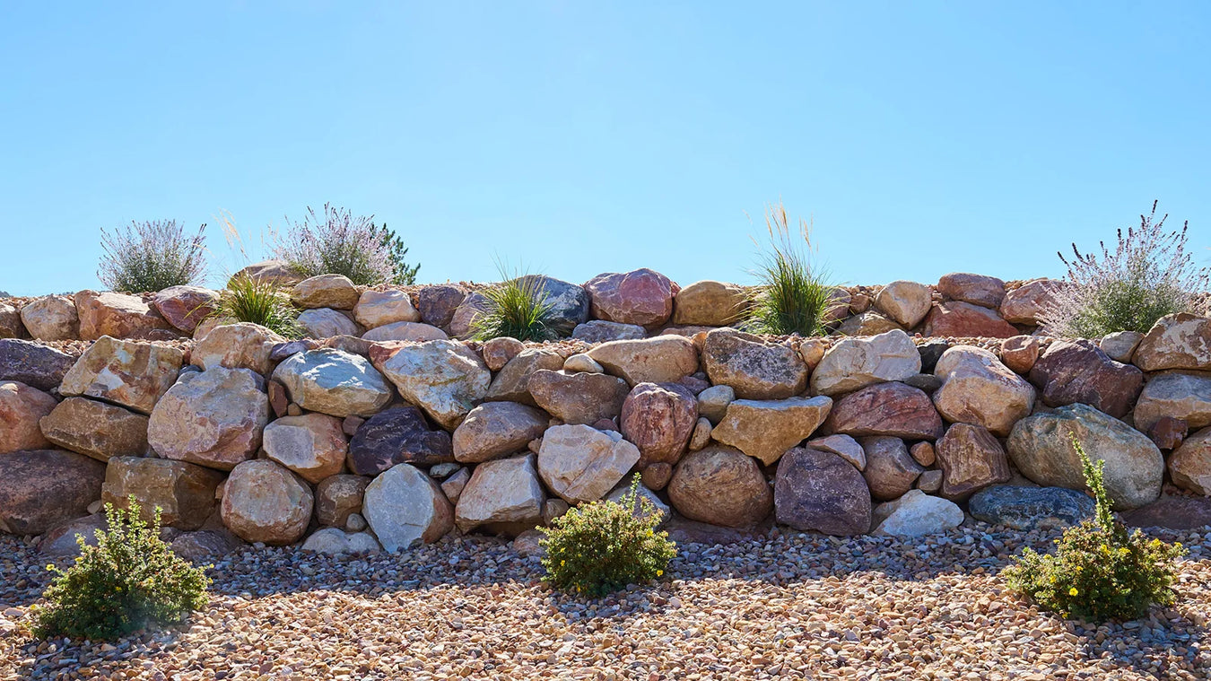 Rock wall with natural stones and small plants against a clear blue sky