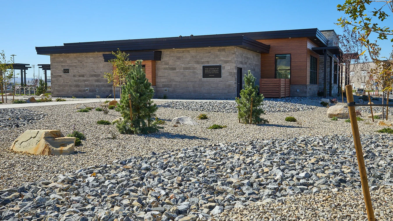 Modern building with a stone facade and wooden accents, surrounded by gravel and small trees.
