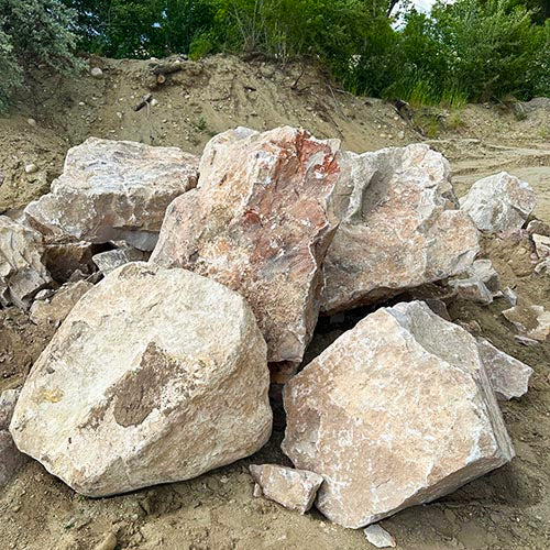 Mountain Rose boulders on a dirt surface with greenery in the background