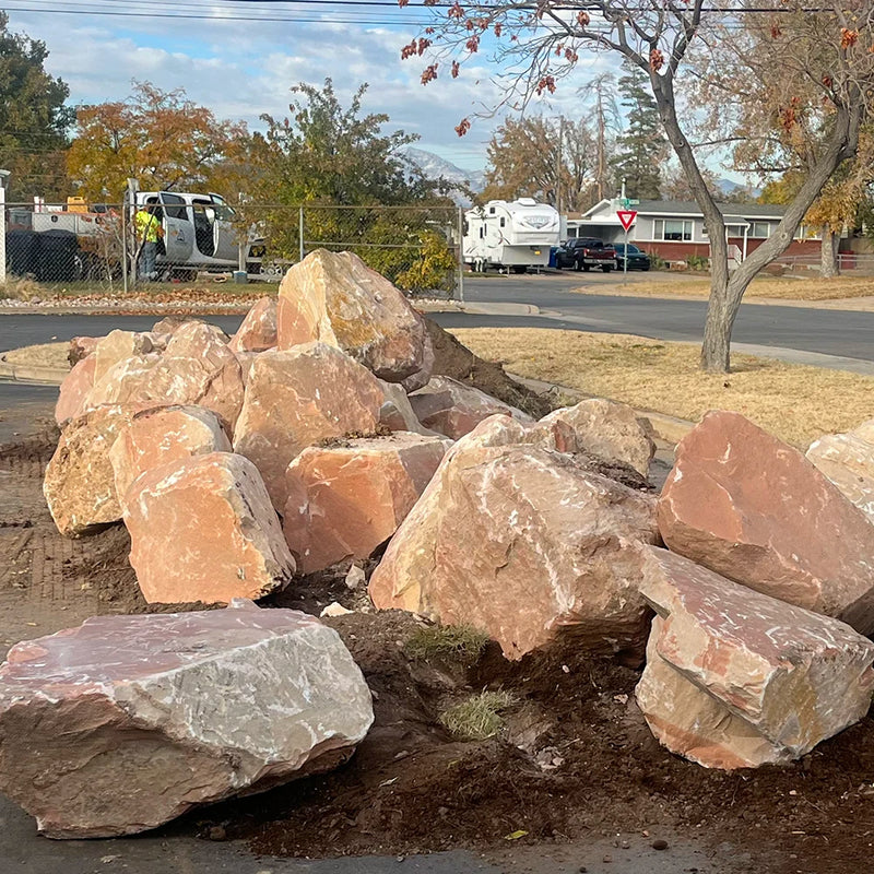 Red Vein boulders on a street corner with vehicles and houses in the background