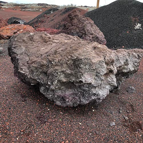 Large lava boulder on a reddish-brown surface with other rocks in the background